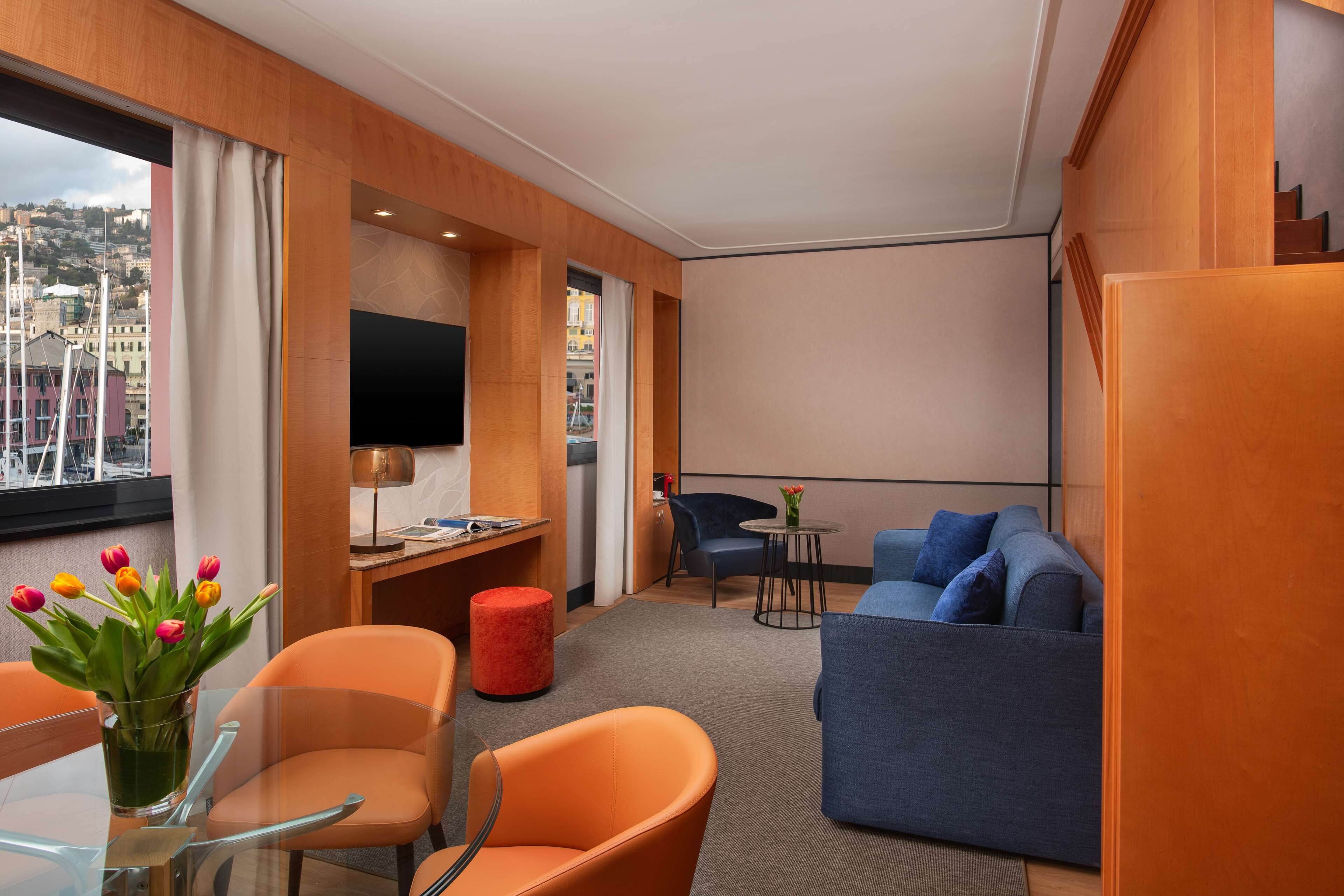 A modern hotel room with a seating area, a TV, and a window with a city view.