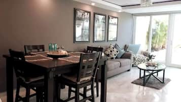 A dining area with a dark wooden table and chairs, a sofa with patterned cushions, and a glass coffee table.