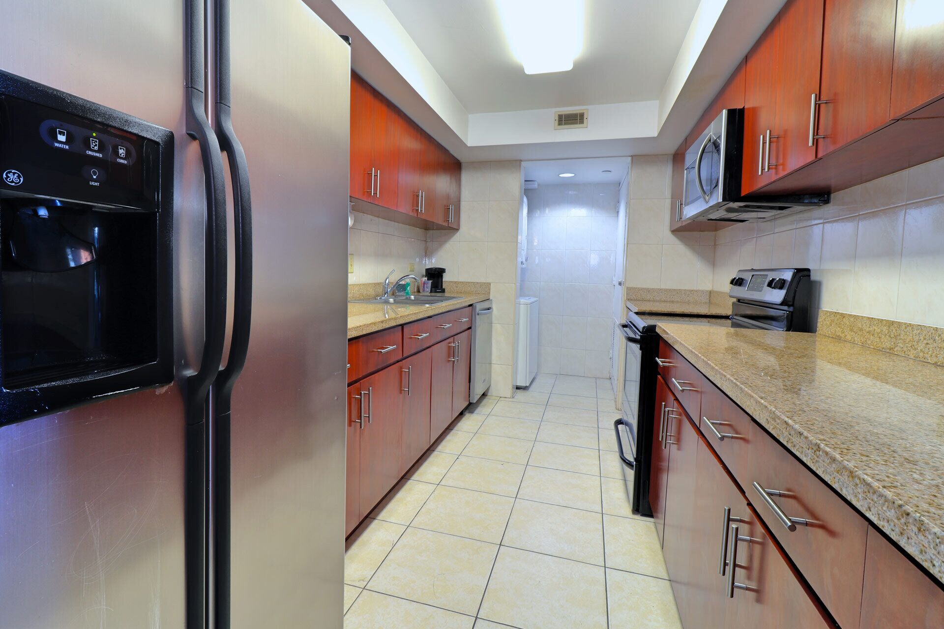 A kitchen with stainless steel appliances, wooden cabinets, and a tiled floor.