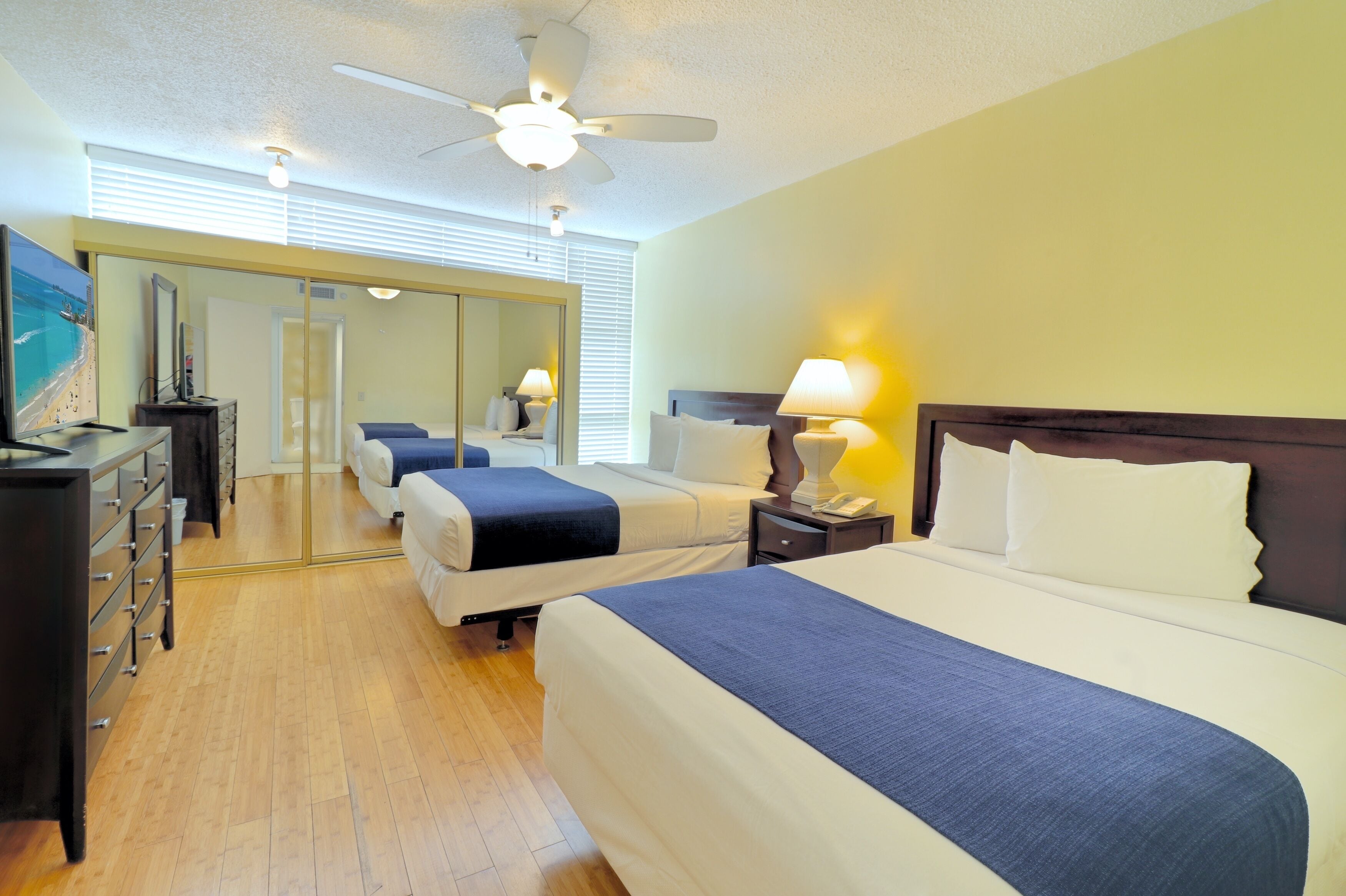 Habitación de hotel con dos camas, ventilador de techo, cómoda y un espejo grande.