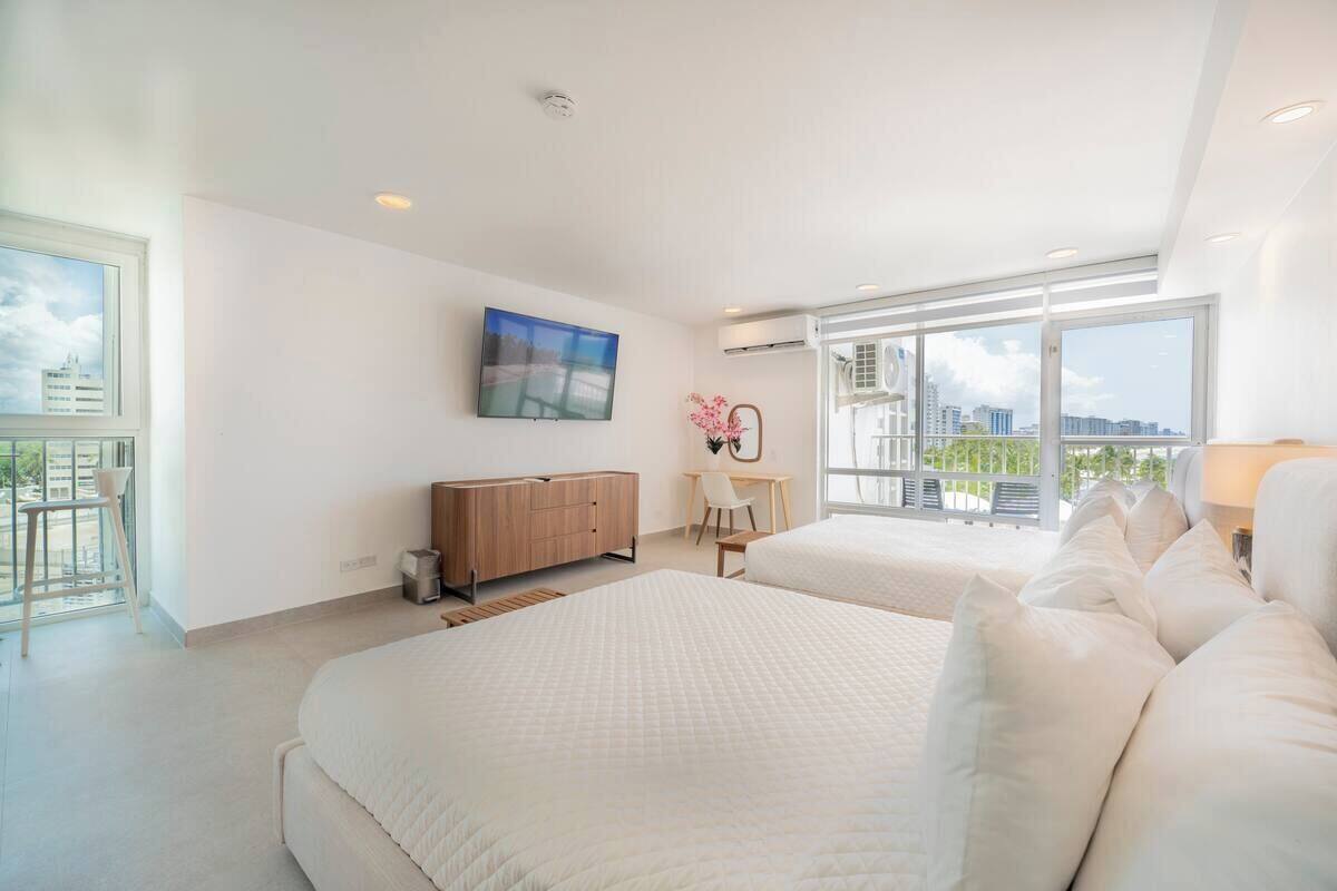 Un dormitorio moderno con dos camas, un escritorio y un amplio ventanal con vistas a la ciudad.