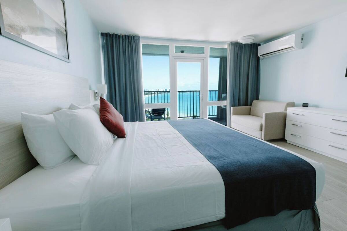 Una habitación de hotel moderna con cama, sofá, escritorio y balcón con vista al mar.