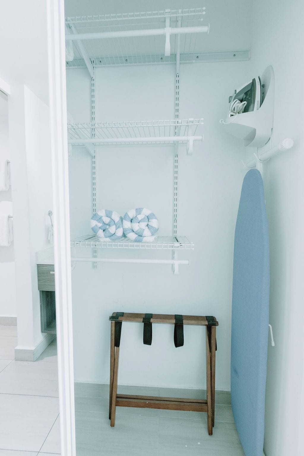 A laundry area with shelves, an ironing board, and a bench.