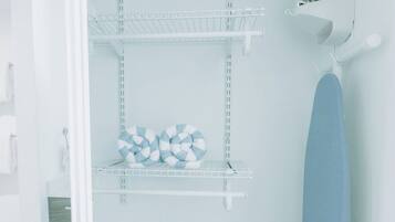A laundry area with shelves, an ironing board, and a bench.