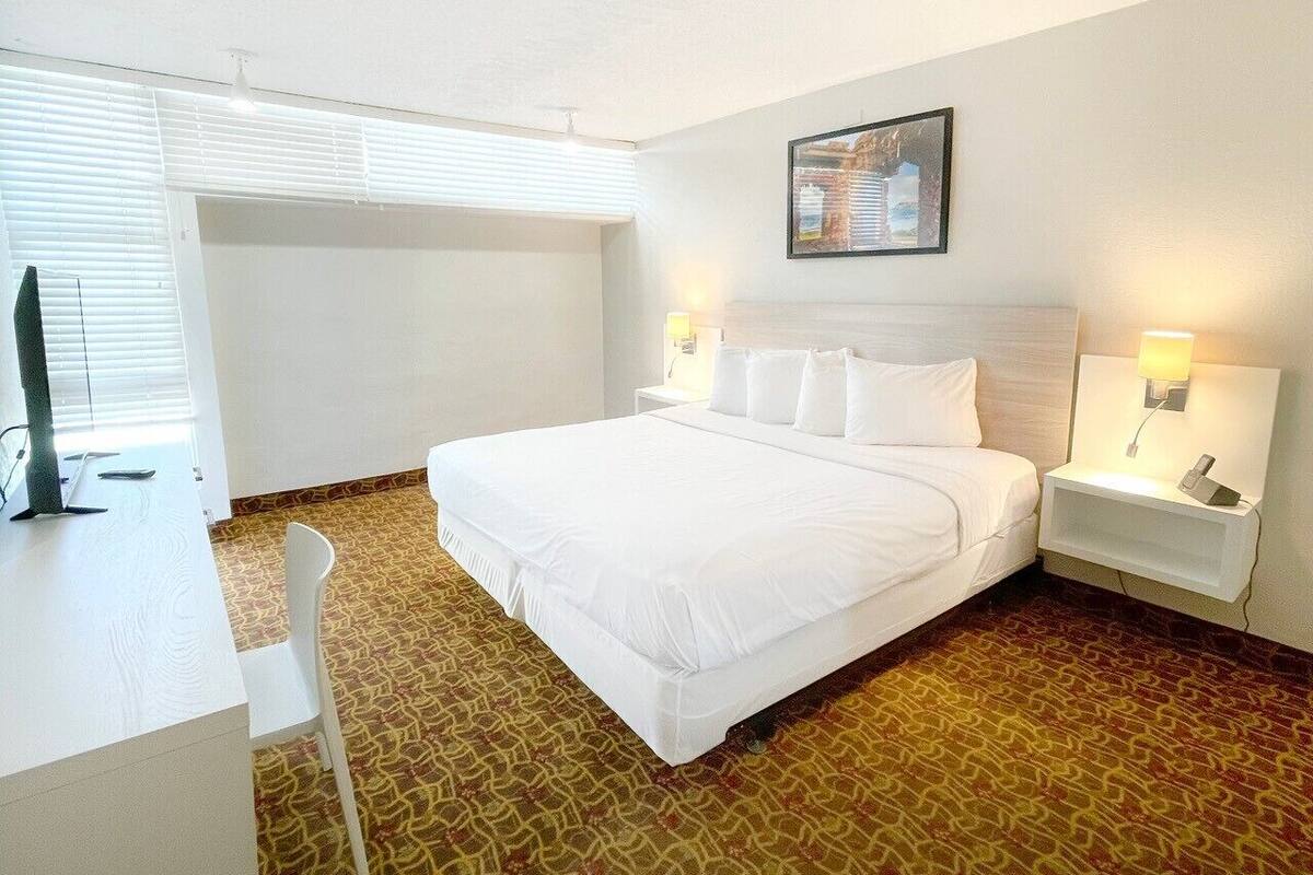Una habitación de hotel con una cama grande, mesitas de noche con lámparas, un escritorio y una silla.