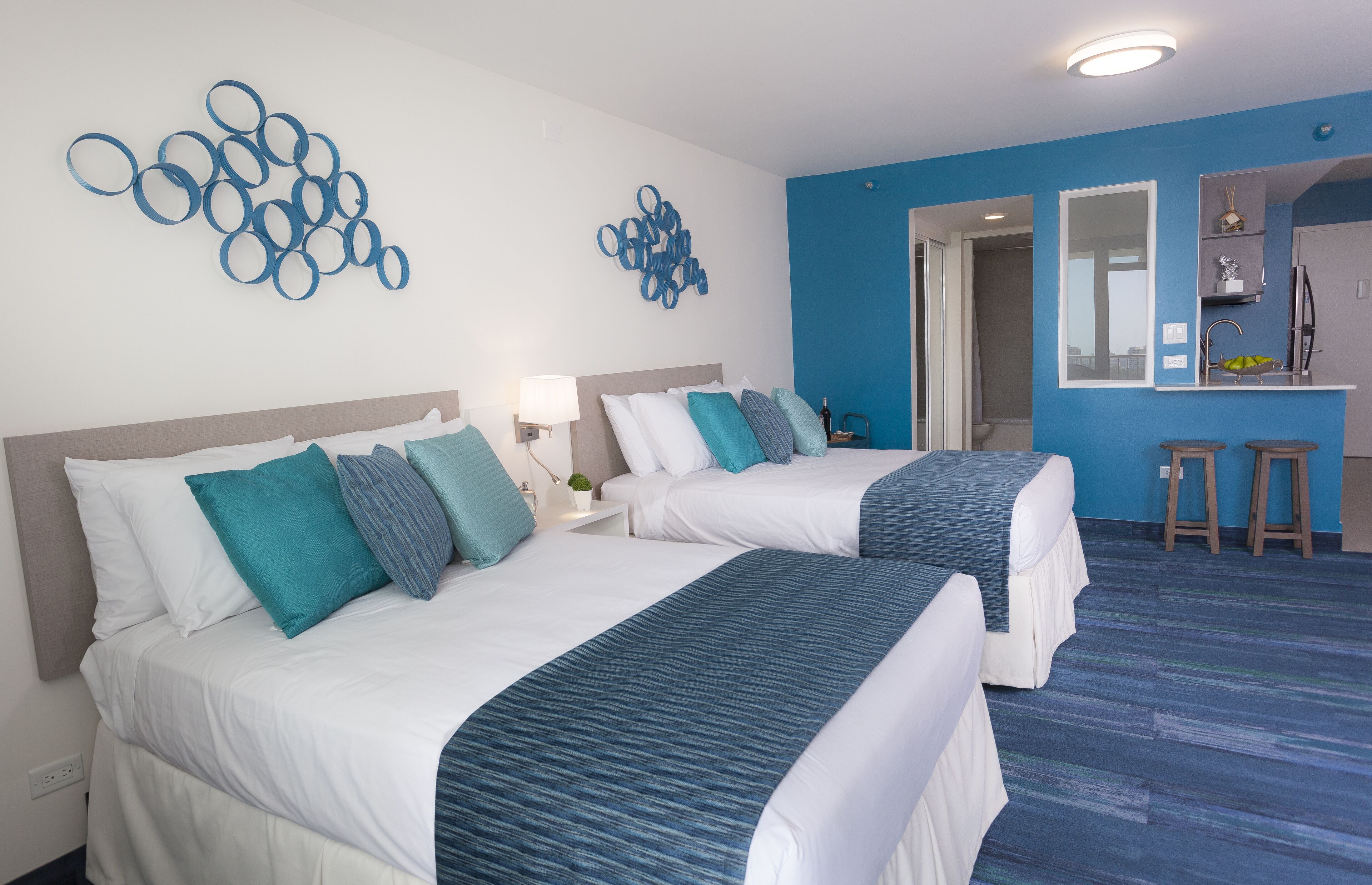 A hotel room with two beds, a small kitchenette, and a bathroom visible through an open door.
