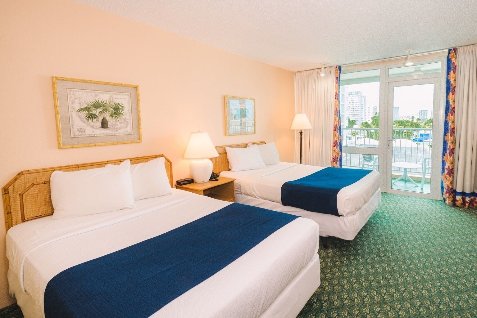 A hotel room with two beds, a balcony with a view, and a cityscape visible through the window.