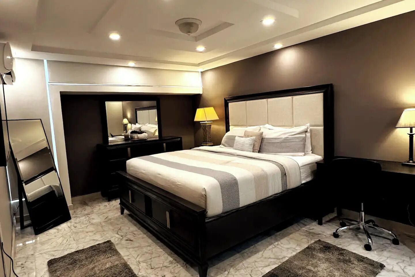 A modern bedroom with a large bed, bedside tables, a desk, and a mirror.