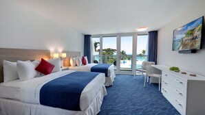 Habitación de hotel con dos camas, un escritorio, una silla y un ventanal con vista al océano.