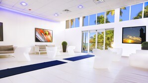 Un moderno vestíbulo de hotel con mobiliario blanco, ventanas amplias y vistas a palmeras.