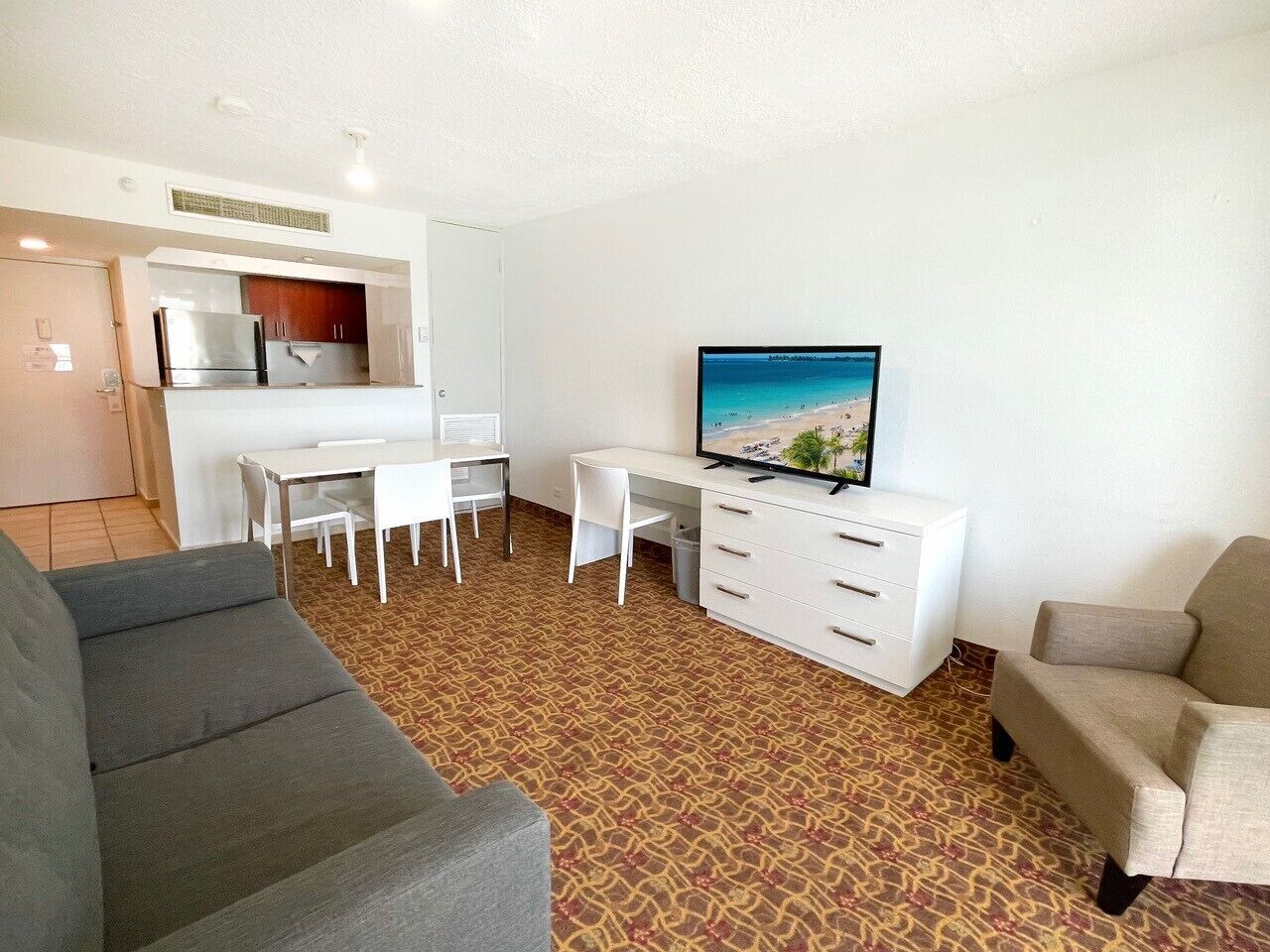 A compact living space with a kitchenette, a flat-screen TV, a dining area, and two sofas.
