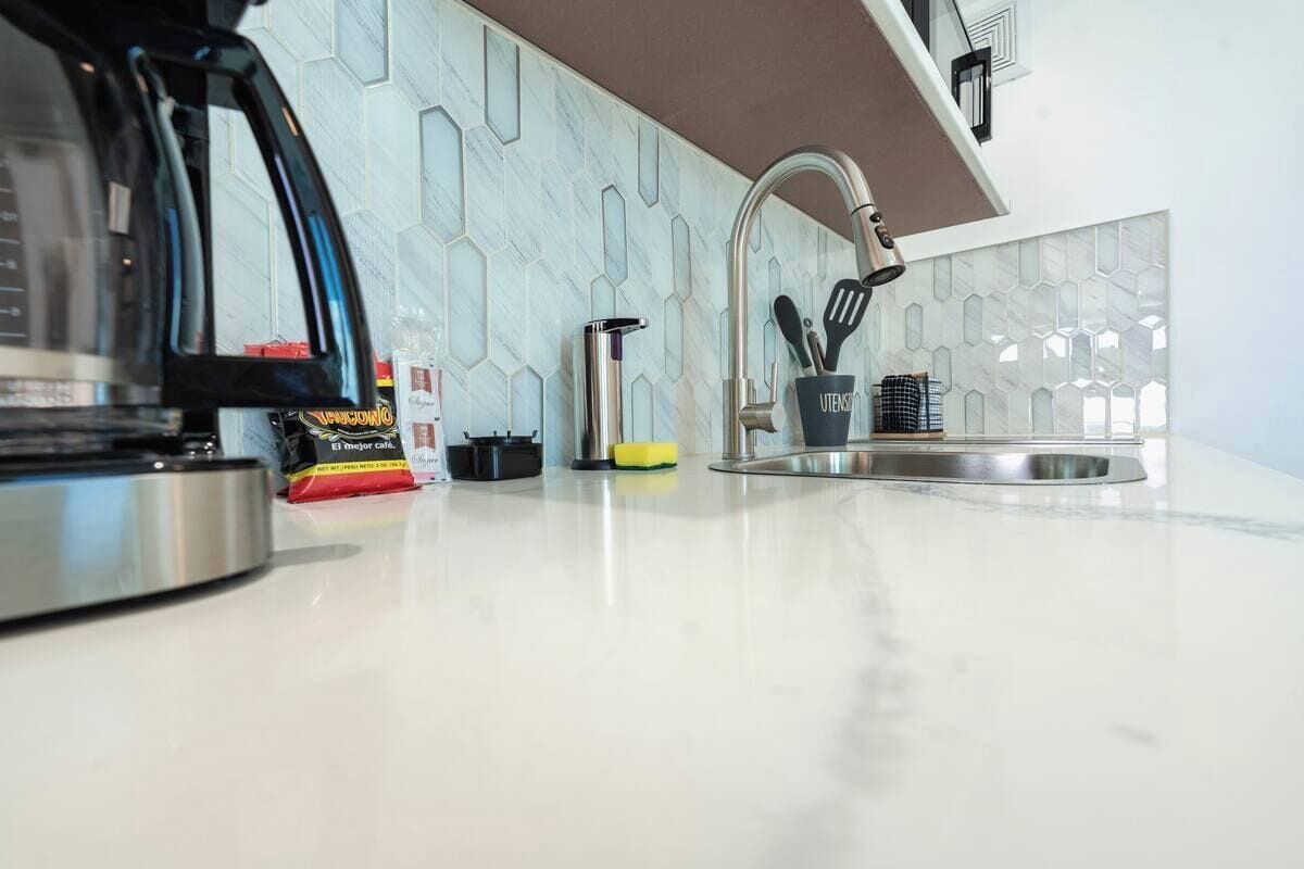 Una cocina con hervidor de acero inoxidable, cafetera, lavabo y un portalapices.