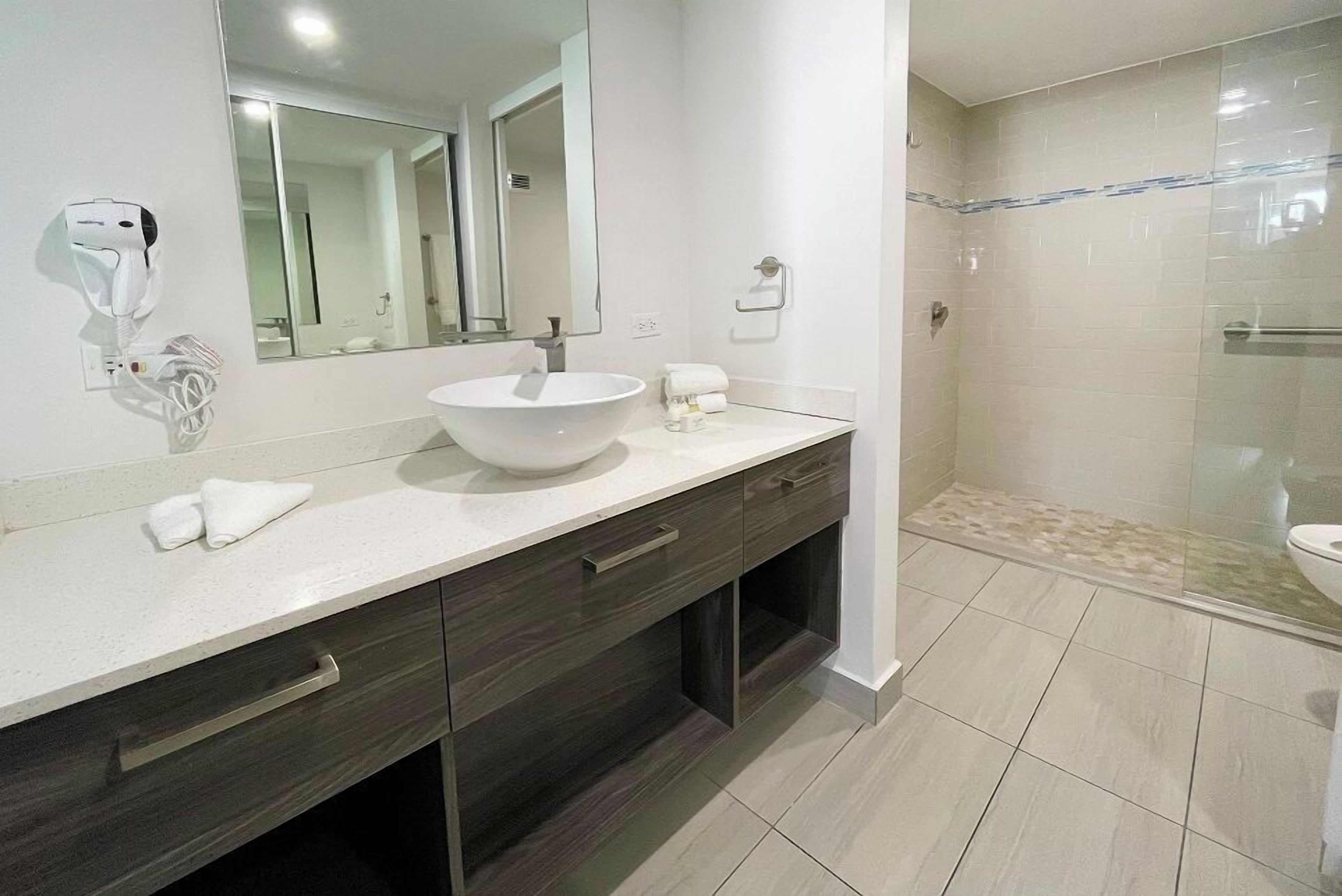 A modern bathroom with a large mirror, a white sink, dark wood cabinets, and a glass shower enclosure.