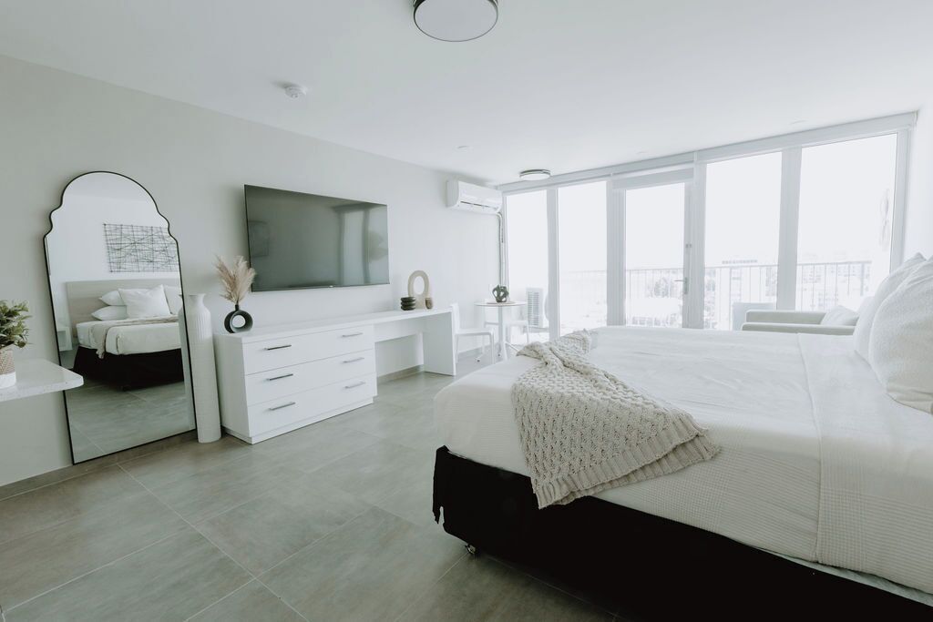 Une chambre moderne avec un grand lit, une télévision, une commode et une grande fenêtre donnant sur la ville.