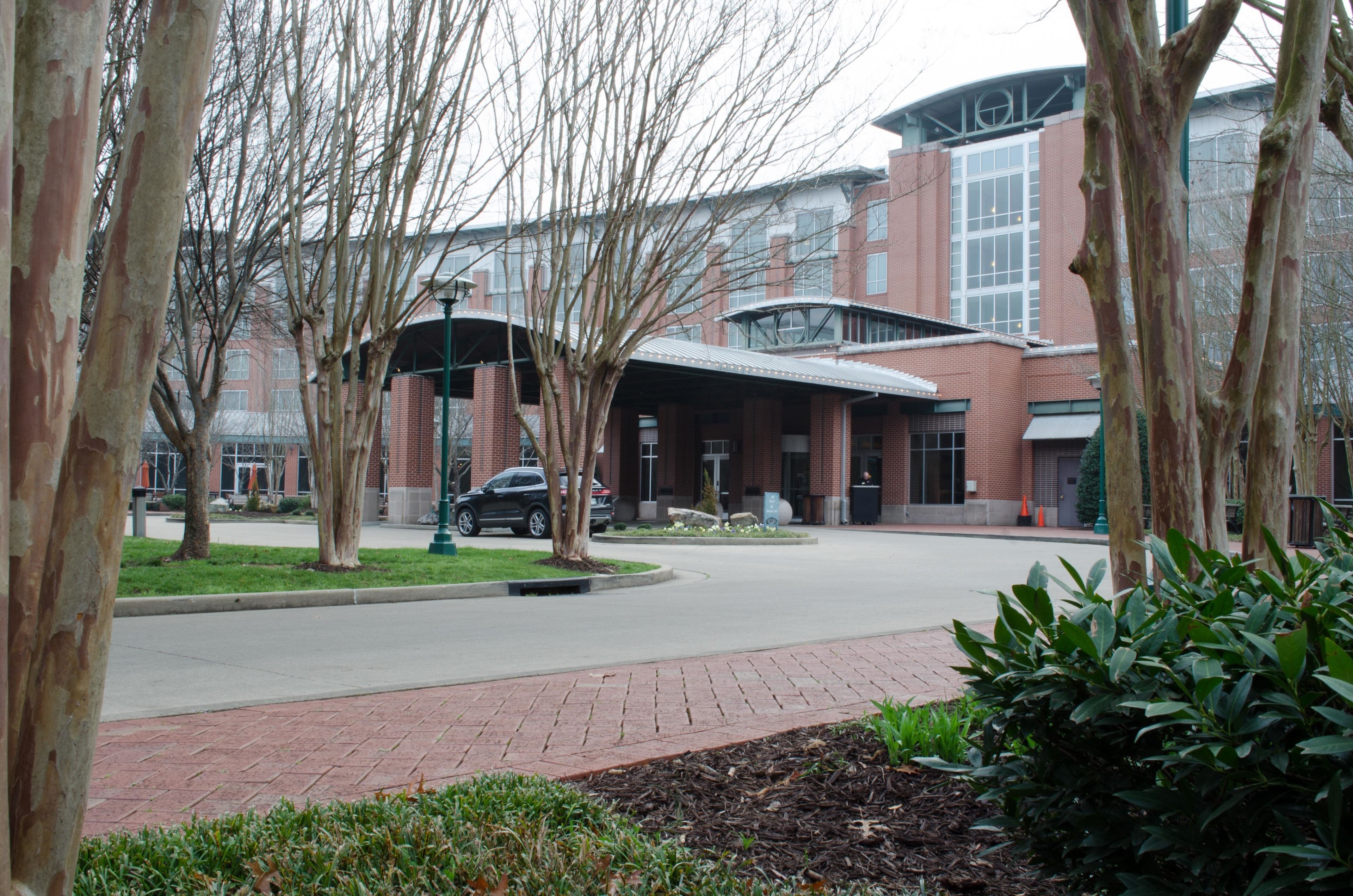 A building with a curved roof and large windows, surrounded by trees and a paved walkway.
