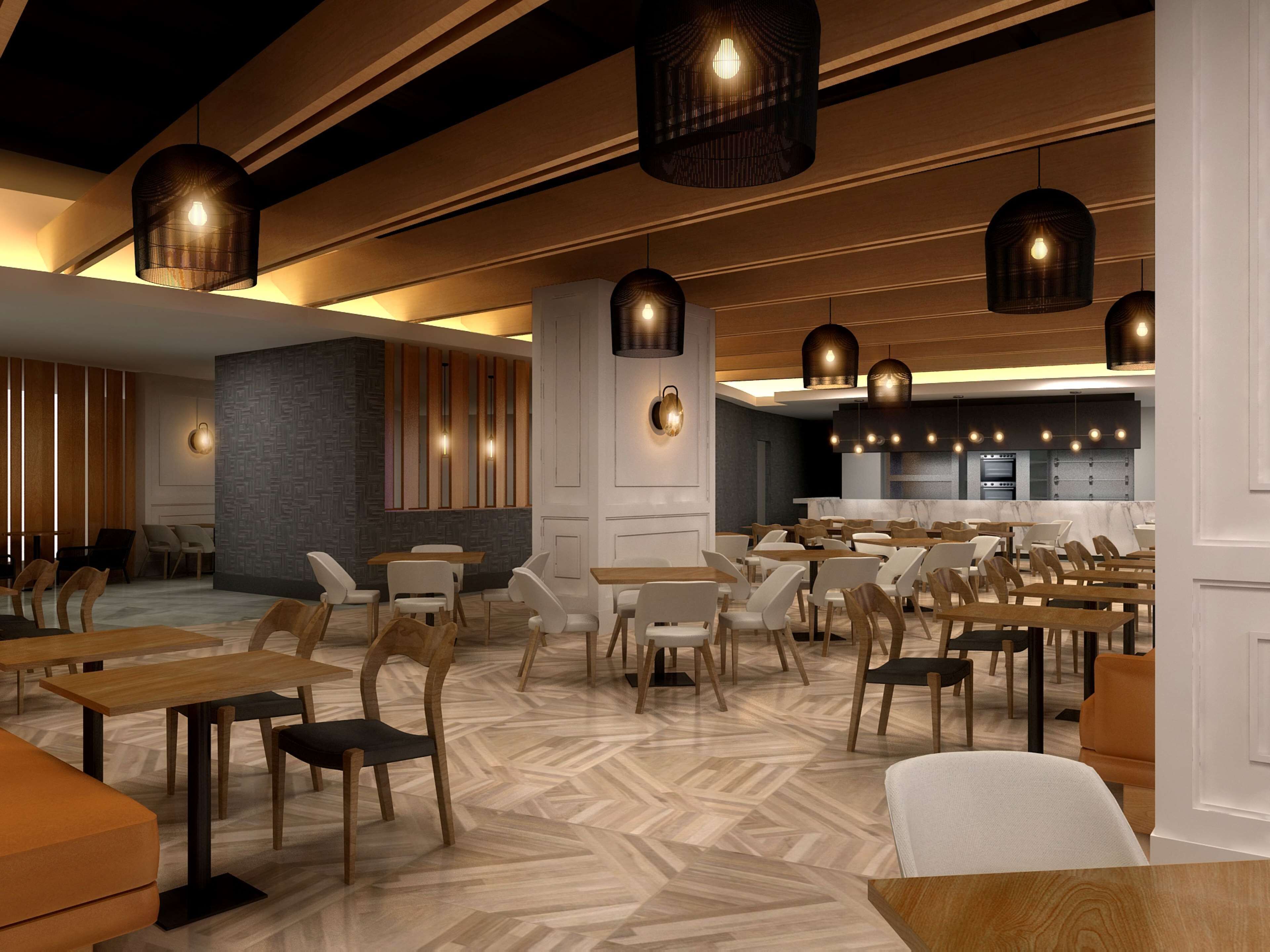 A modern restaurant interior with wooden tables and chairs, pendant lighting, and a herringbone-patterned floor.