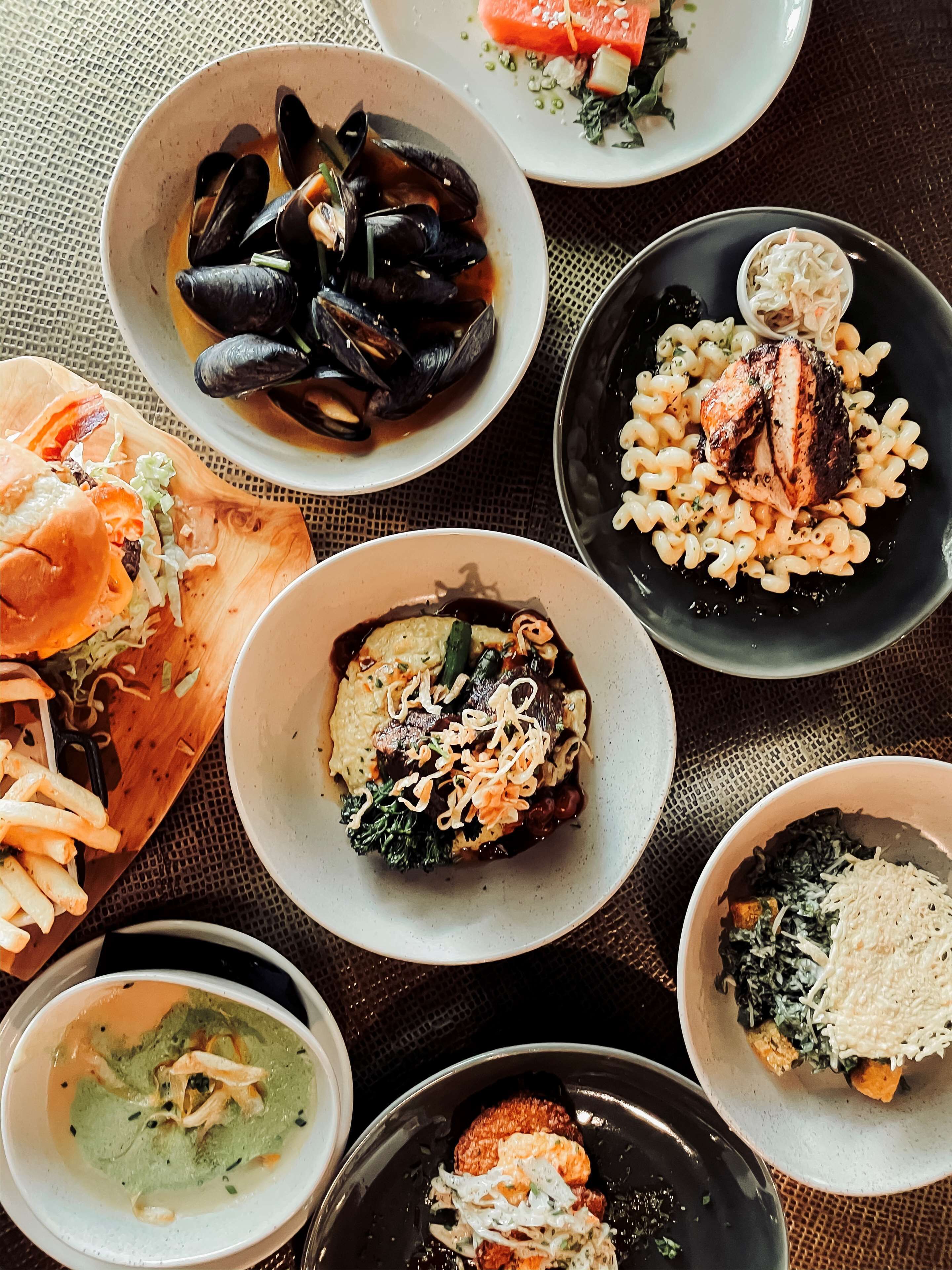 A variety of dishes including mussels, pasta, and a burger, arranged on a table.