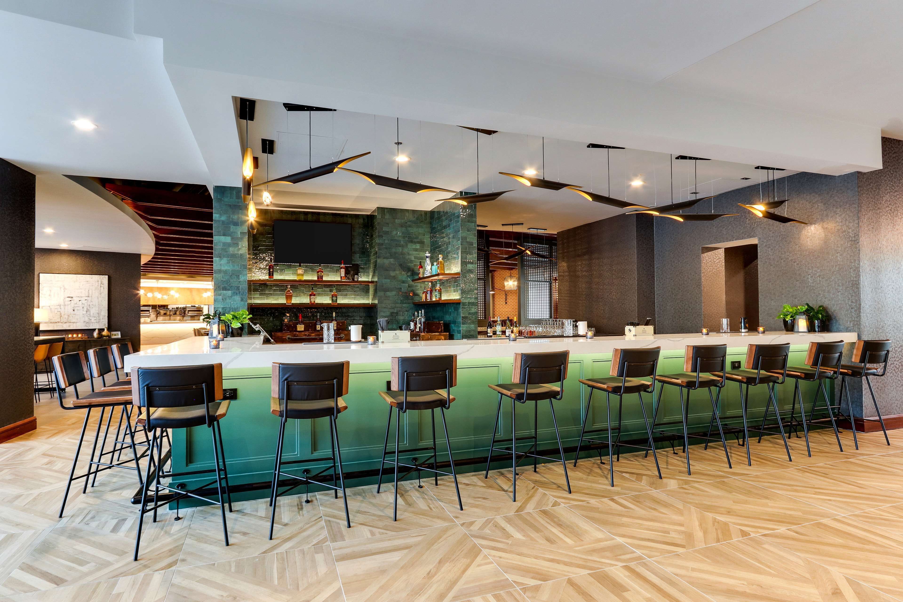 A modern bar area with a long counter, multiple bar stools, and a herringbone-patterned floor.