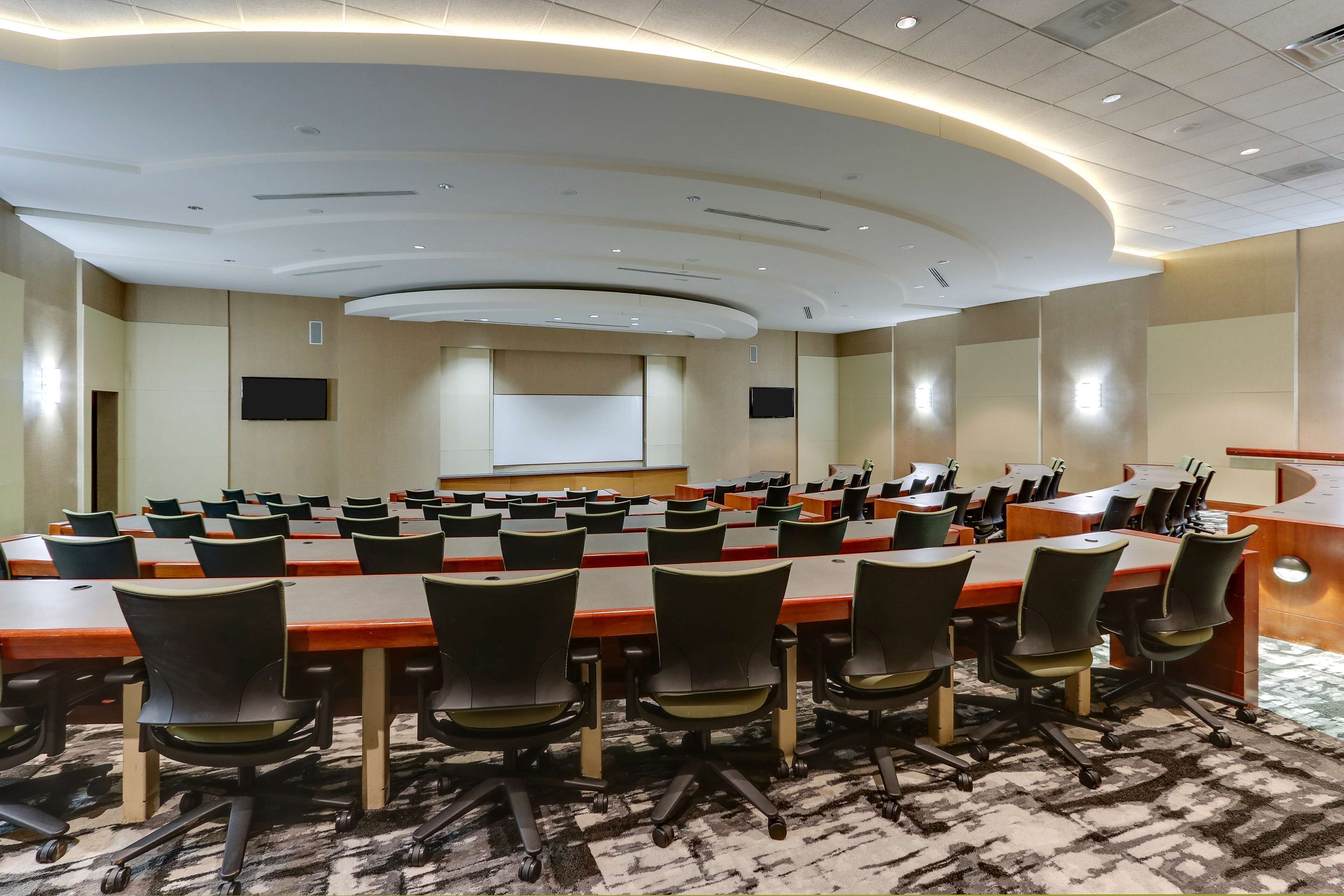 Une salle de conférence équipée de plusieurs tables et chaises, d’un grand écran et d’un pupitre.