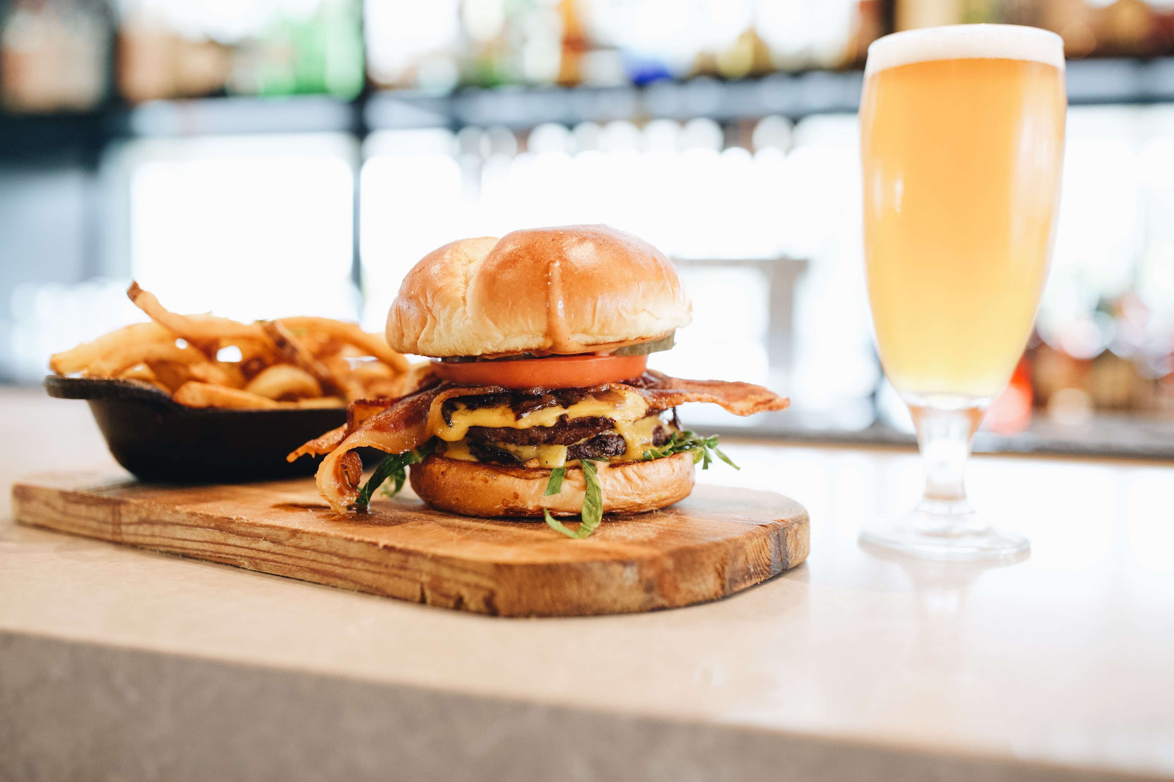 Un hamburger con patatine fritte e un bicchiere di birra su un tagliere di legno.