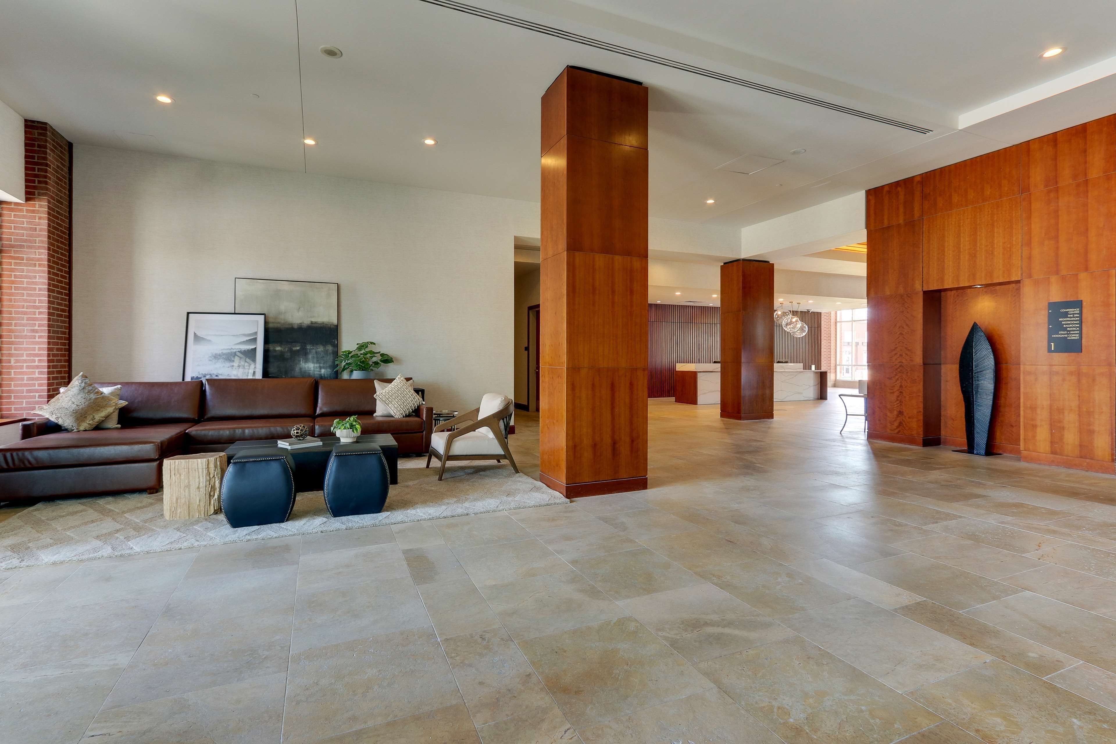 Un hall d’entrée spacieux, avec un canapé en cuir marron, deux poufs ronds bleus et un comptoir d’accueil en bois.