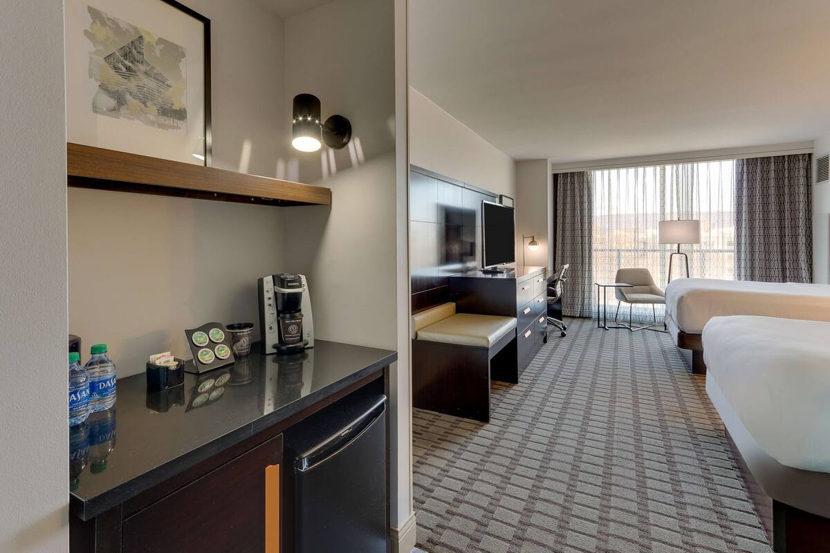 A hotel room with a bed, a desk with a chair, a TV, a coffee maker, and a minibar.