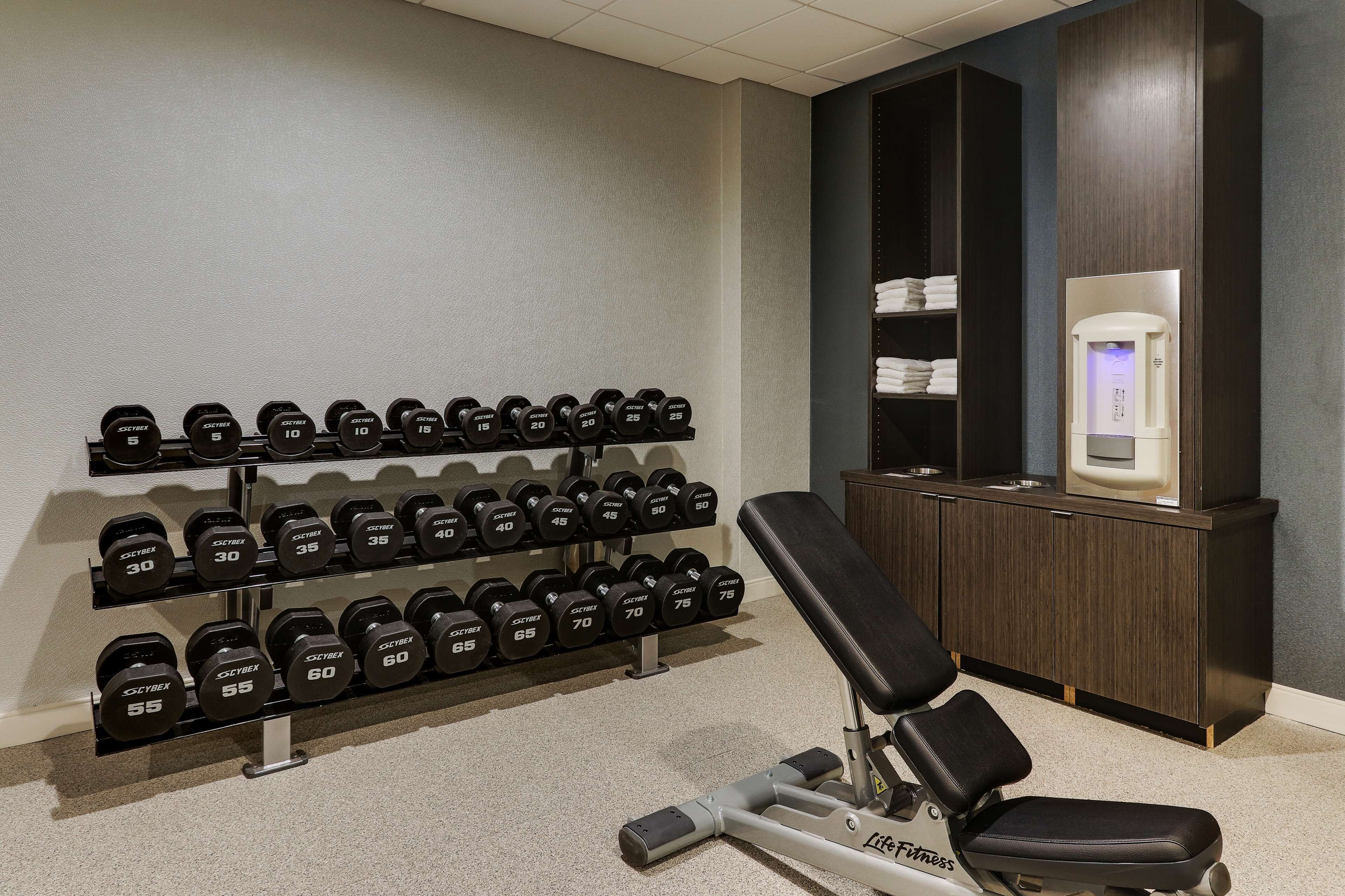 A gym with weight racks, a bench, and a water dispenser.
