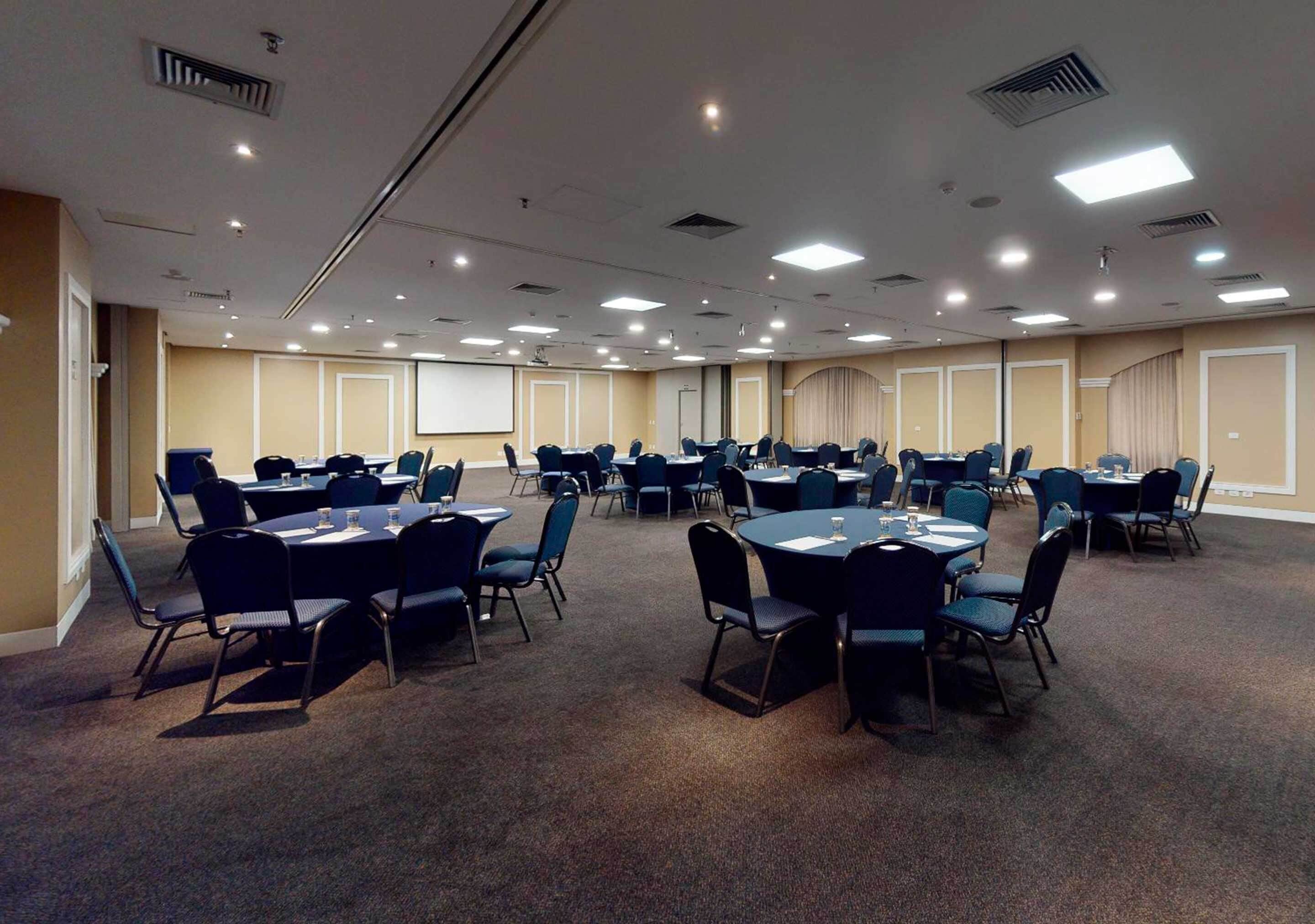 A conference room with multiple tables and chairs, equipped with projectors and screens.