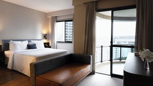Habitación de hotel con una cama grande, un sofá, un escritorio y un balcón con vistas a la ciudad.
