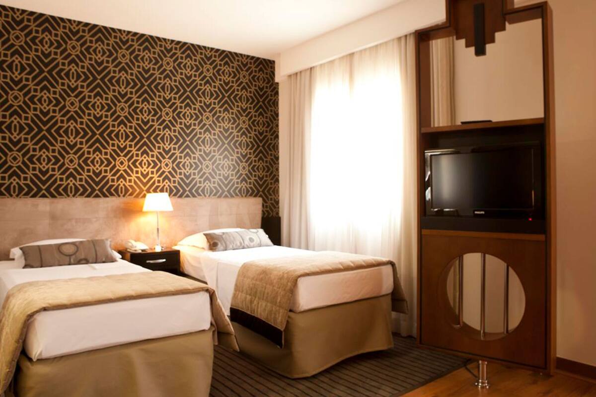 Quarto de hotel com duas camas, uma televisão e parede com padrão.