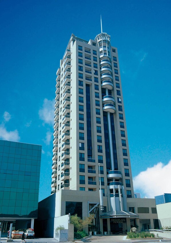 A tall, modern hotel with a central cylindrical tower, multiple balconies, and a prominent entrance.