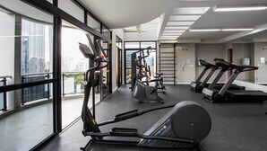 Un gimnasio moderno con cintas de correr, elípticas y equipo de pesas. Amplias ventanas ofrecen vistas de la ciudad.