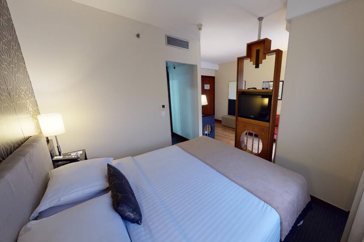 Quarto de hotel com cama, abajur e televisão.
