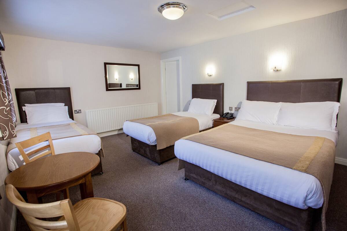 A hotel room with three beds, a wooden table, and a chair.