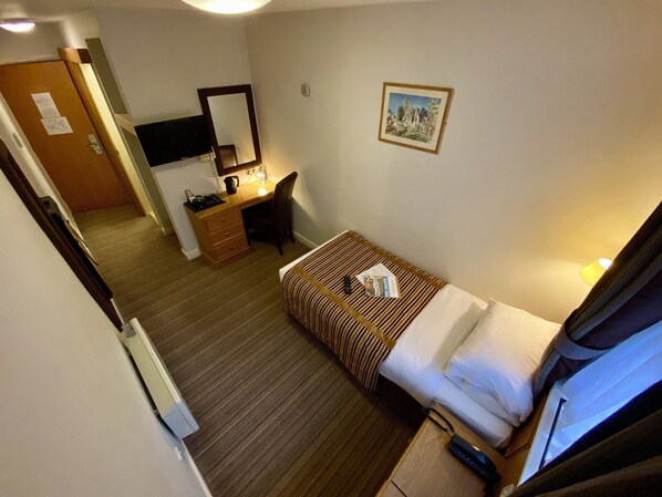 A hotel room with a bed, a desk, a chair, a mirror, and a picture on the wall.