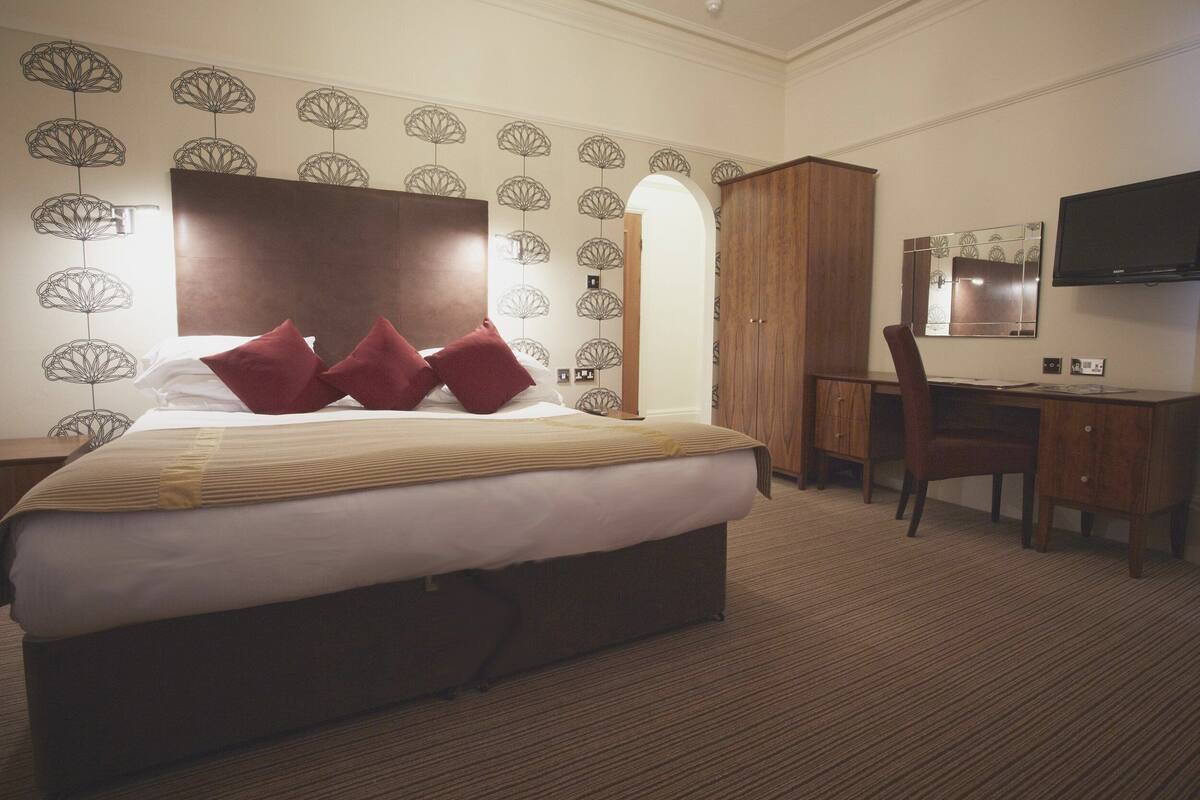 A hotel room with a large bed, a desk, a chair, and a television.