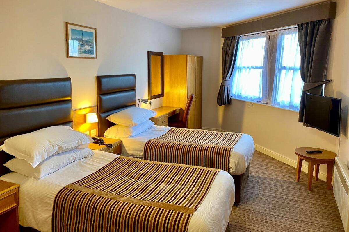 A hotel room with two beds, a desk, a chair, a TV, and a window with curtains.