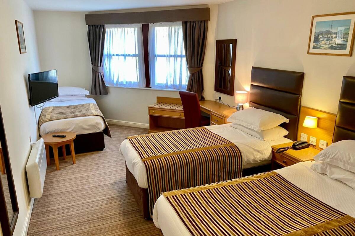 A hotel room with two beds, a desk, a chair, a TV, and a window with curtains.