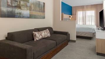 A hotel room with a sofa, a bed, a TV, and a painting on the wall.
