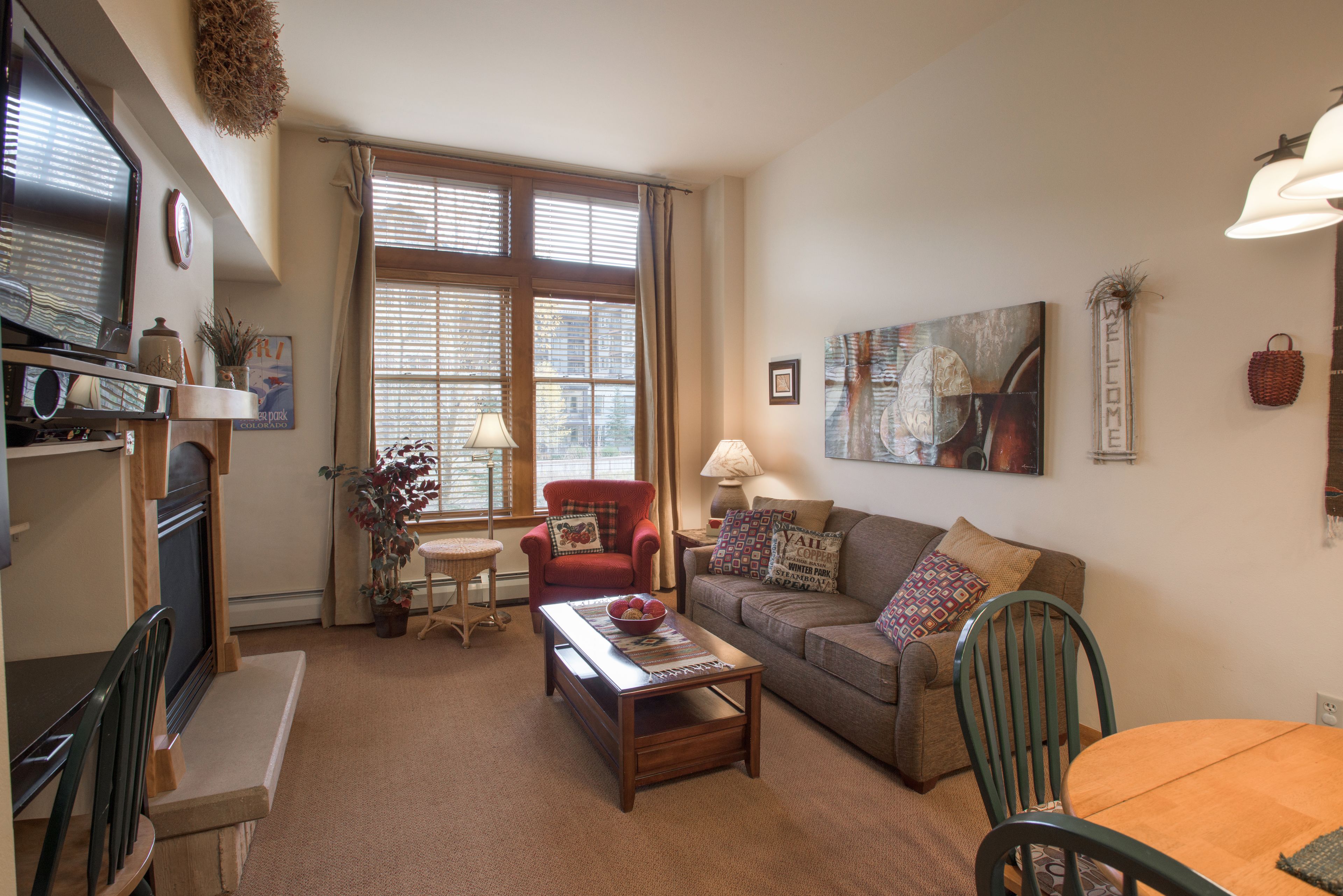 A cozy living room with a fireplace, a dining area, and a large window with blinds.