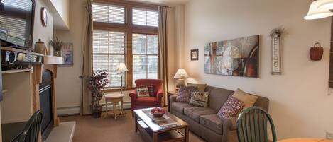 A cozy living room with a fireplace, a dining area, and a large window with blinds.