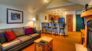 A cozy living room with a sofa, a coffee table, and a kitchen area with bar stools. - Zephyr Mountain Lodge (Winter Park)