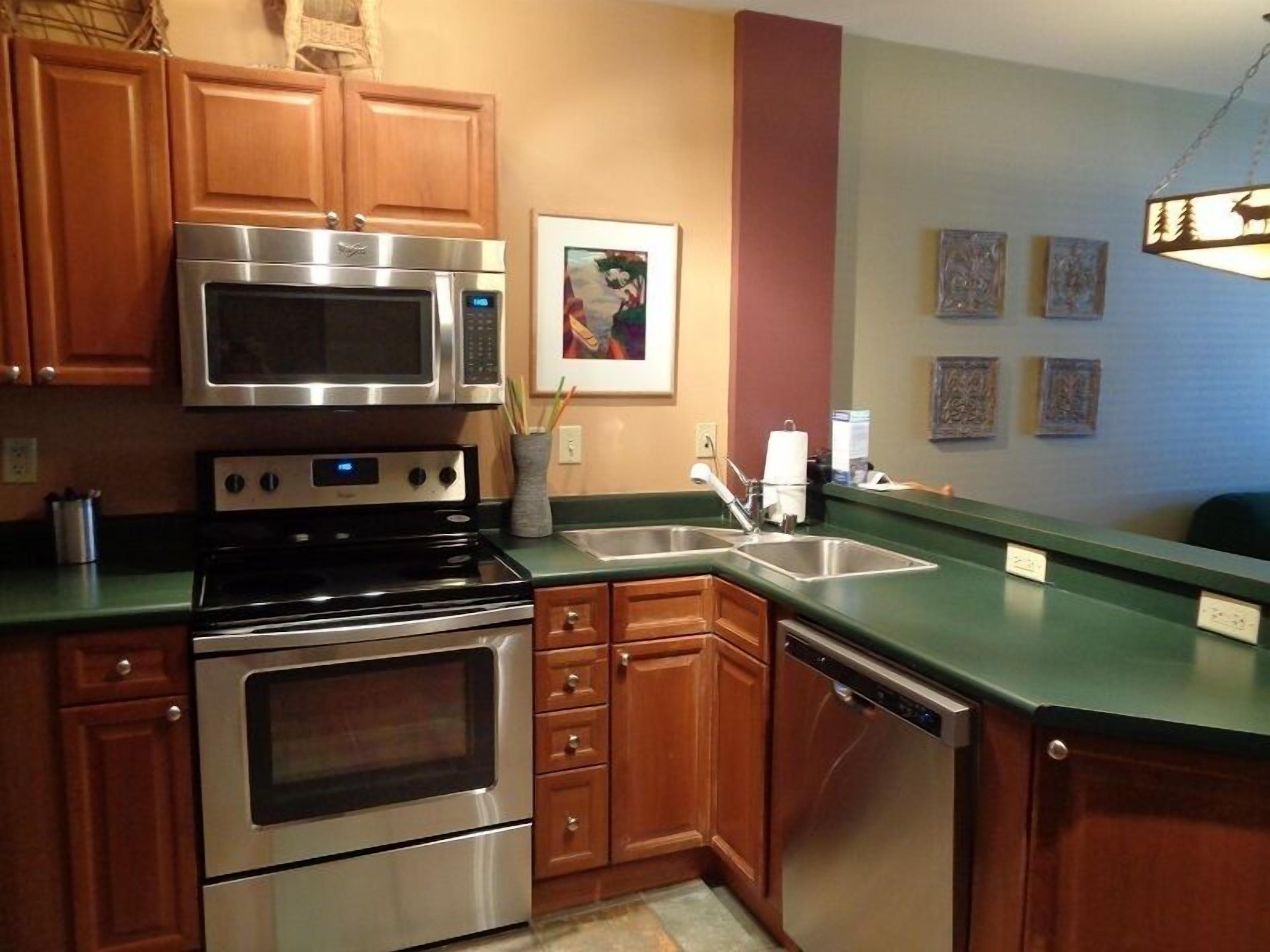 A kitchen with wooden cabinets, stainless steel appliances, a green countertop, and a wall-mounted light fixture.