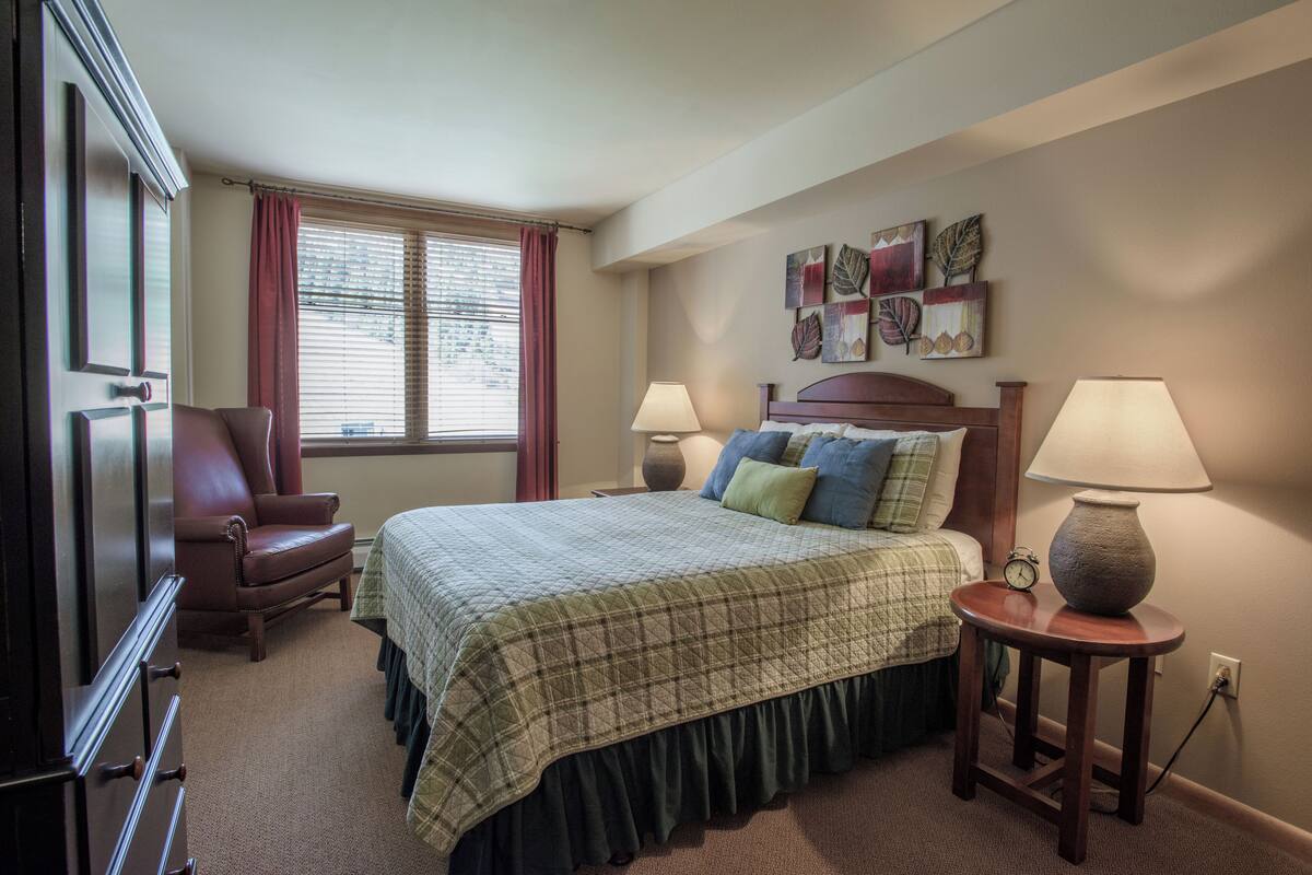 A neatly arranged bedroom with a bed, two bedside lamps, a chair, and a wall clock.