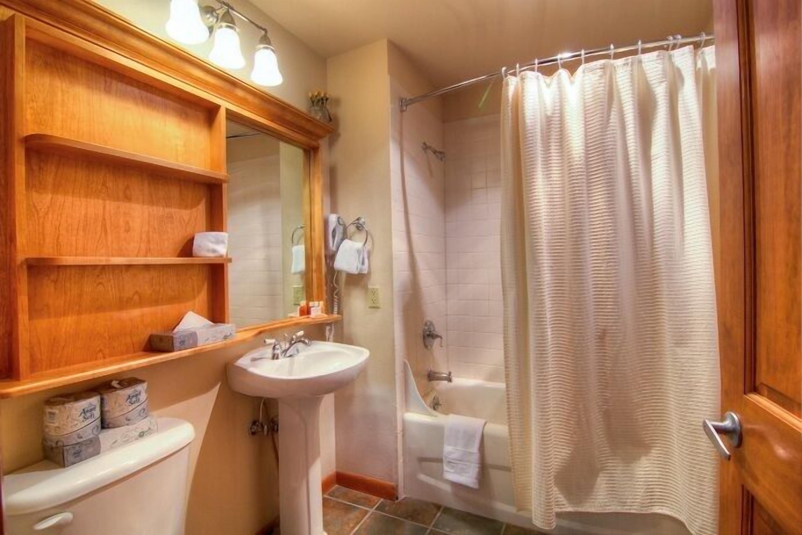 A bathroom with a wooden vanity, a sink, a toilet, a bathtub, and a shower curtain.