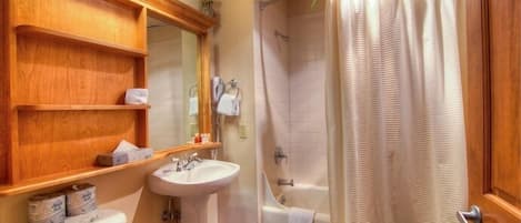 A bathroom with a wooden vanity, a sink, a toilet, a bathtub, and a shower curtain.