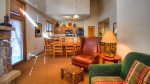 A spacious living room with a fireplace, a green sofa, a leather armchair, and a dining area with wooden chairs and a table. - Zephyr Mountain Lodge (Winter Park)