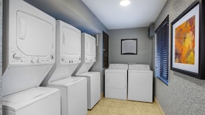 Une buanderie équipée de quatre machines à laver et de quatre sèche-linge, avec un sol carrelé et un panneau encadré accroché au mur.