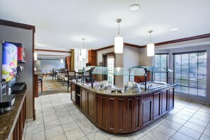 Un espace pour le petit-déjeuner à l’hôtel, comprenant un buffet, un coin salon et de grandes fenêtres.