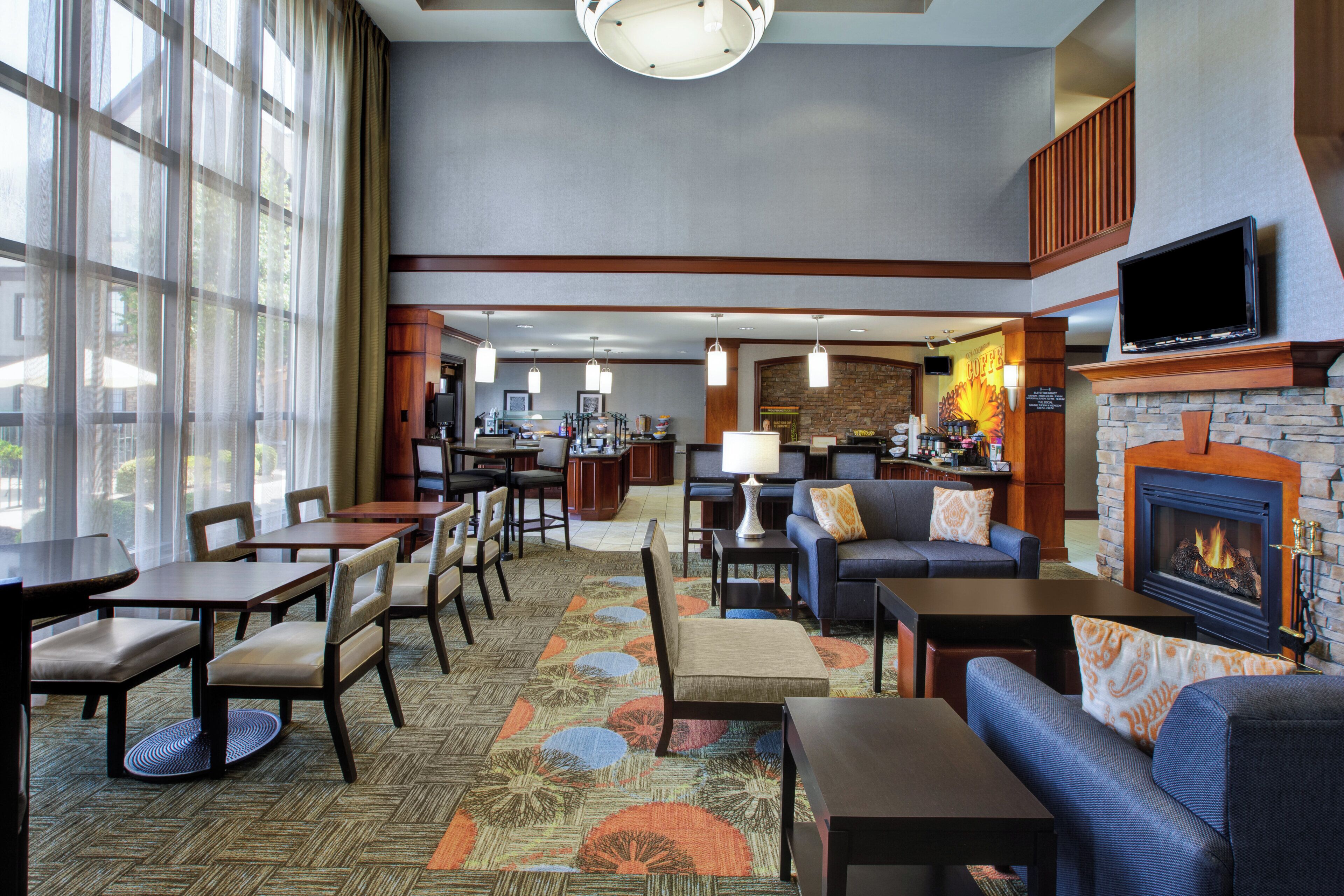A hotel lobby with a dining area, seating, a fireplace, and a television.